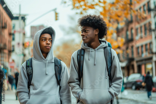 Two Afroamerican teenagers boys in blank hoodies walking in city street photo