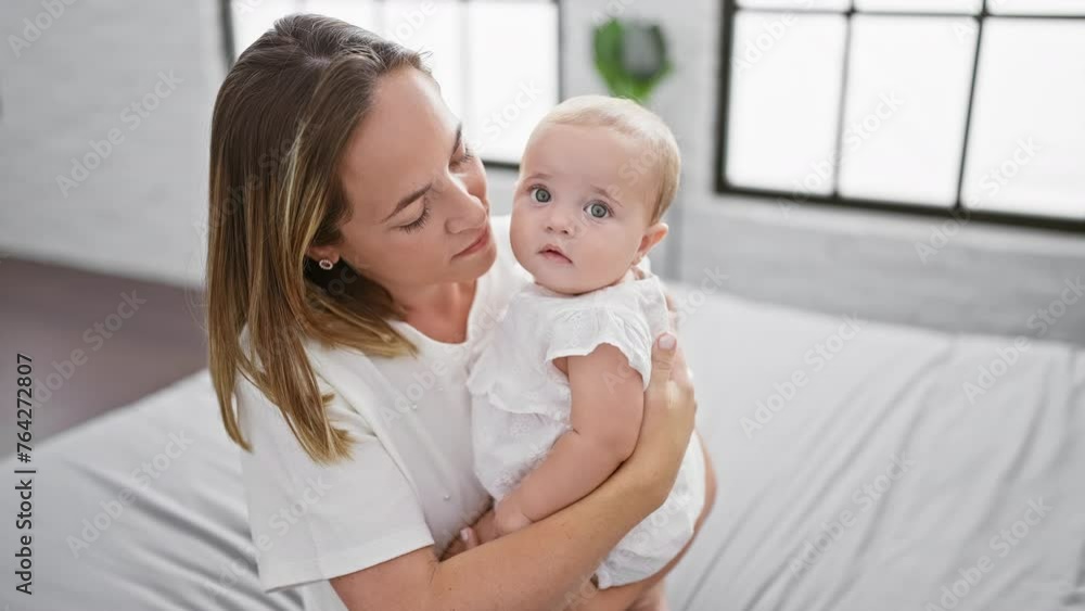 Joyful mother hugging and kissing daughter, enjoying a casual and fun moment sitting on bed in cozy bedroom, expressing confident love and positive family relationship.