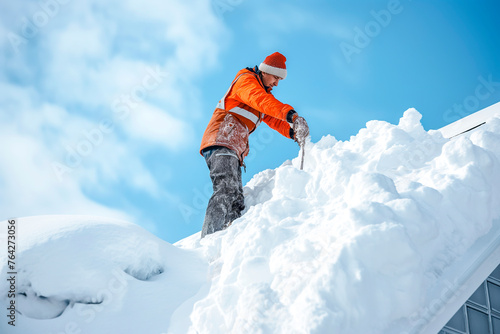 Worker cleans snow on the roof. Male worker clearing snow off roof of a house after big blizzard. Safety at home in winter conditions. Blue sky photo