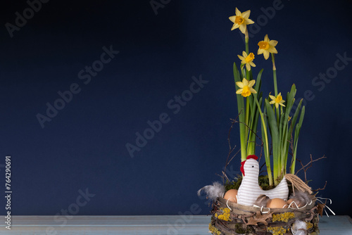 Easter decor in rustic style. Nest, chicken, yellow daffodils on navy blue background.Handmade.Concept of home comfort and decor on  bright holiday of Easter. Copy cpase. Close-up.