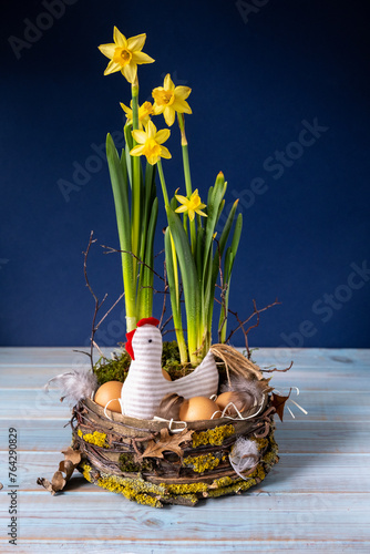 Easter decor in rustic style. Nest, chicken, yellow daffodils on navy blue background.Handmade.Concept of home comfort and decor on  bright holiday of Easter. Vertical