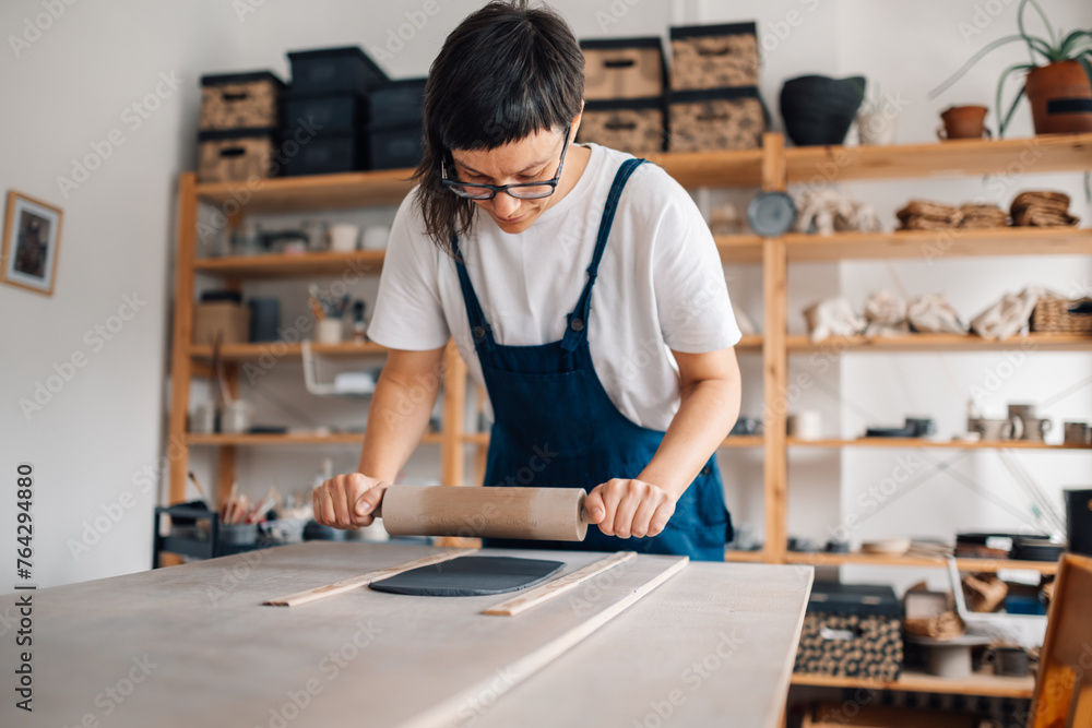 A potter using rolling pin for modeling wet clay at ceramic studio.