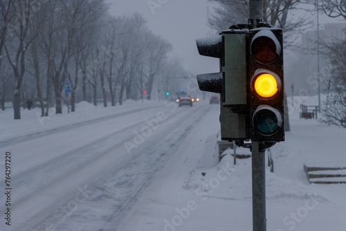 Winter bad weather condition. Traffic light on the street. Yellow light. Blurred background