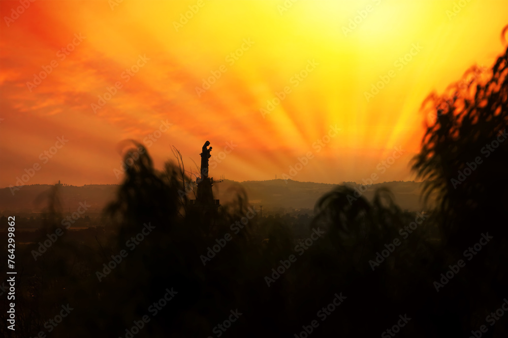Our blessed virgin Mary, with her son in her arms, prays for sinners, against the light, against a background of sunset lights. Our blessed virgin Mary, with her son in her arms, prays for sinners, against the light, against a background of sunset lights.