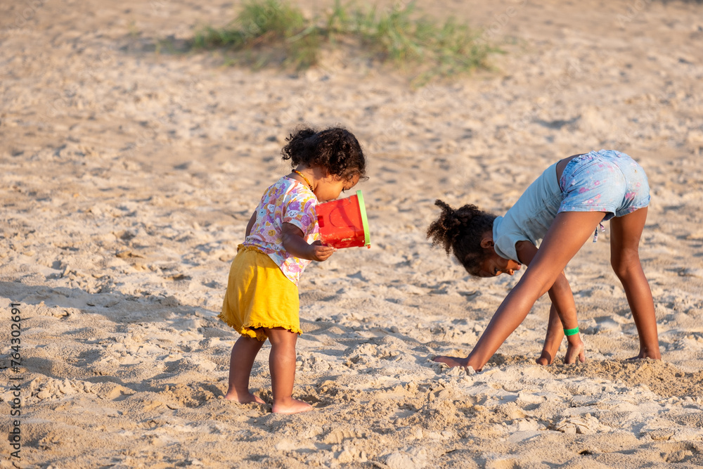 Two children, sisters, play independently with sand toys on a beach, a scene of shared yet individual play, national siblings day and playing in nature. Two children, sisters, play independently with sand toys on a beach, a scene of shared yet individual play, national siblings day and playing in nature.