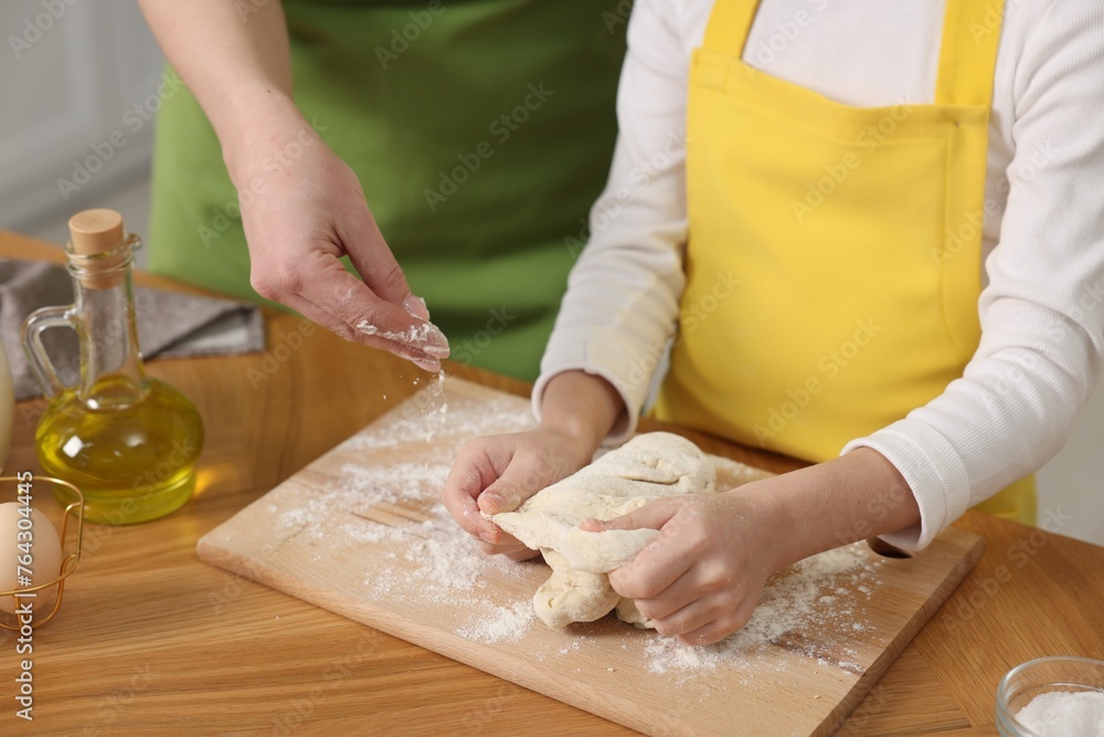 Making bread. Mother and her daughter kneading dough at wooden table indoors, closeup