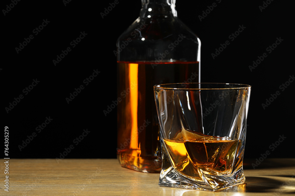 Whiskey in glass and bottle on wooden table against black background. Space for text Whiskey in glass and bottle on wooden table against black background. Space for text