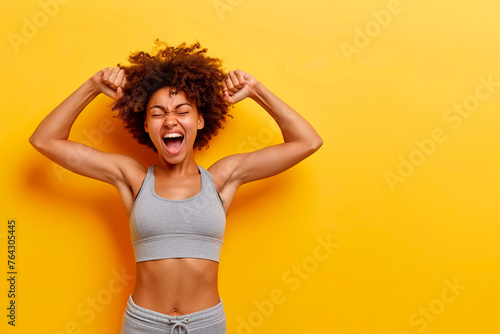 An Afro woman with a big smile on her face is doing a fist pump, yellow background photo