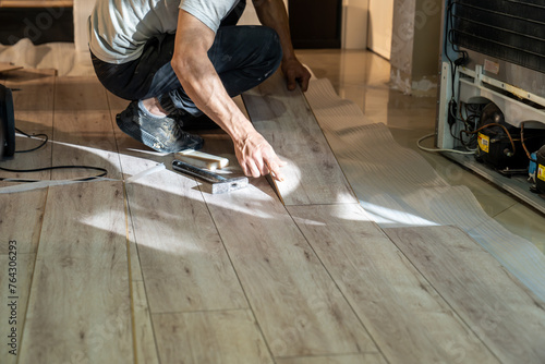 Laminate master man laying wooden laminate parquet on the floor. Home renovation with ceramic floors.