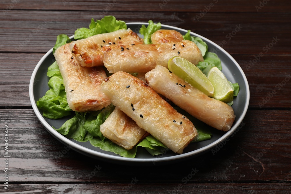 Tasty fried spring rolls, lettuce and lime on wooden table Tasty fried spring rolls, lettuce and lime on wooden table