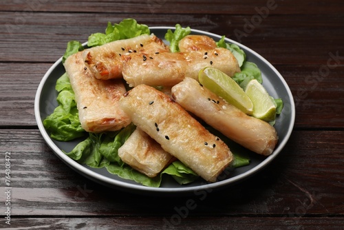 Tasty fried spring rolls, lettuce and lime on wooden table