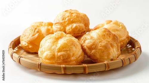A group of five whole golden profiteroles baked and served on a bamboo plate, isolated against a photo