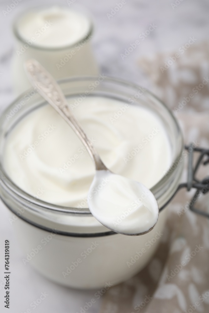 Delicious natural yogurt in glass jar and spoon on table, closeup Delicious natural yogurt in glass jar and spoon on table, closeup