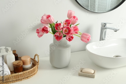 Vase with beautiful pink tulips and toiletries near sink in bathroom