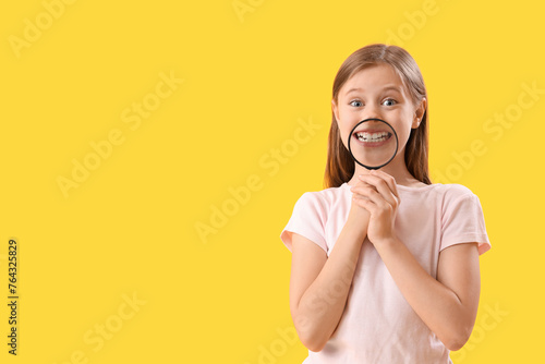 Little girl with magnifier on yellow background