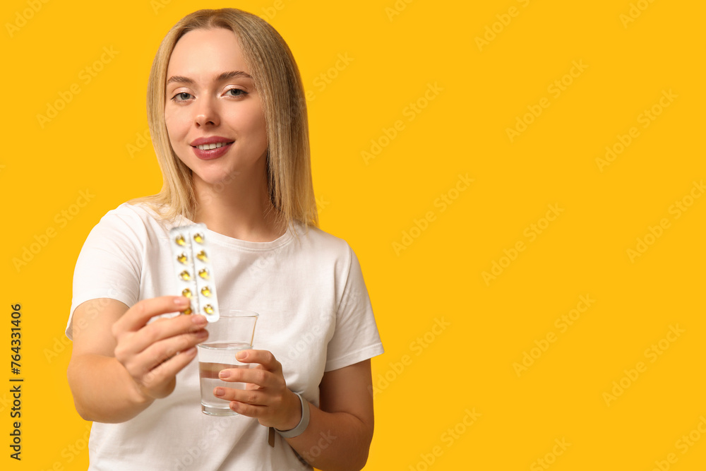 Young woman with vitamin A pills and glass of water on yellow background Young woman with vitamin A pills and glass of water on yellow background