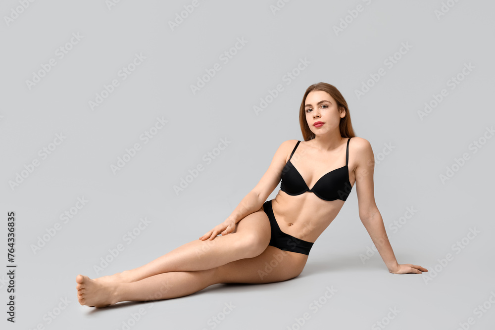 Fototapeta premium Sexy young woman in black underwear sitting against light background