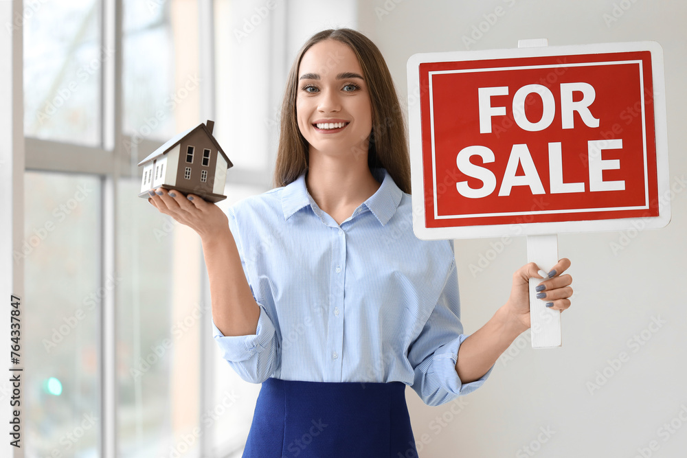 Portrait of female real estate agent with house model and FOR SALE sign in new apartment Portrait of female real estate agent with house model and FOR SALE sign in new apartment