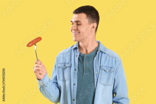 Young man with tasty sausage on yellow background