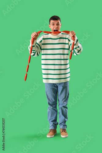 Young man eating tasty sausages on green background