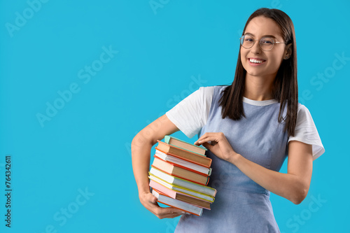 Young woman in eyeglasses with stack of books on blue background