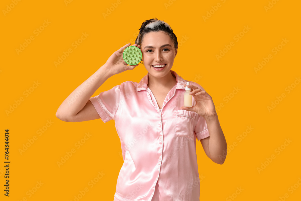 Beautiful young woman with hair scalp massager and bottle of cosmetic oil on yellow background Beautiful young woman with hair scalp massager and bottle of cosmetic oil on yellow background