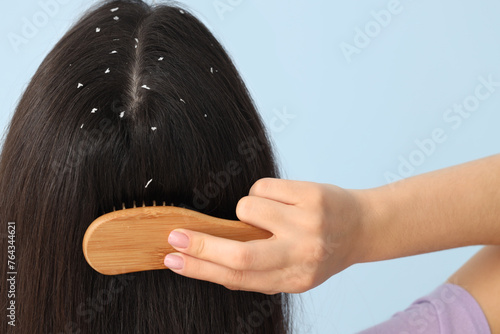 Young woman with dandruff problem combing hair on blue background, back view