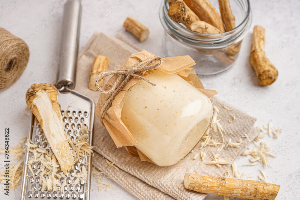 Jar of horseradish sauce with horseradish roots on white background