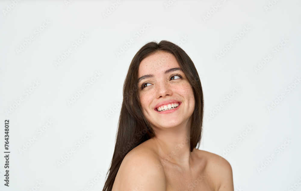 Obraz premium Happy brunette Latin girl isolated on white background. Smiling pretty young adult Hispanic woman with freckles on face looking away at copy space advertising skincare, hair skin care beauty products.