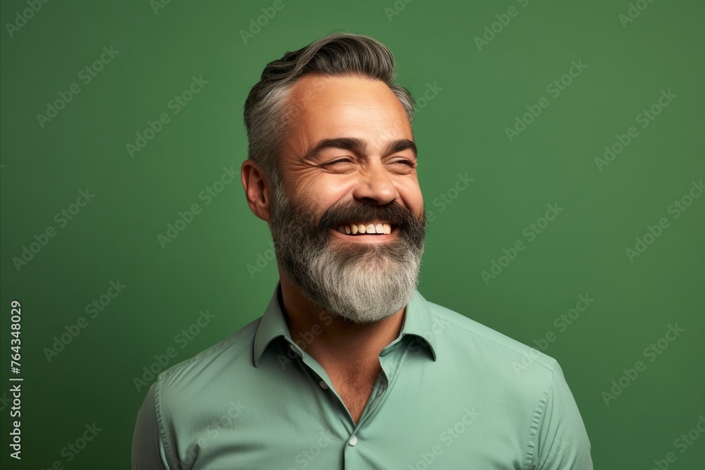 Portrait of a handsome mature man with grey beard and mustache smiling against green background