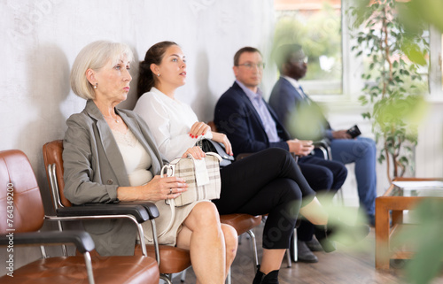 Elderly woman in business suit waiting for her turn on chair in reception
