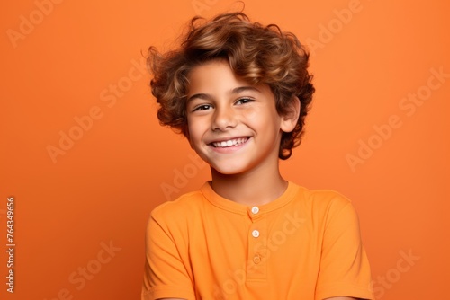 Portrait of a smiling little boy with curly hair on orange background
