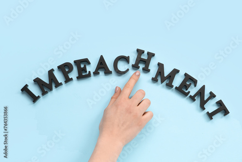 Female hand with black letters spelling word IMPEACHMENT on blue background