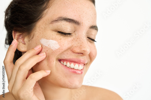Obraz na plátně Beauty shot of happy freckled Latin girl model applying face sunscreen or moisturizer cream for perfect hydrated healthy fresh skin care isolated on white background, skincare treatment, close up