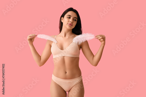 Pretty young woman with soft feathers on pink background. Epilation concept