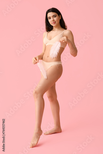 Pretty young woman with soft feathers on pink background. Epilation concept