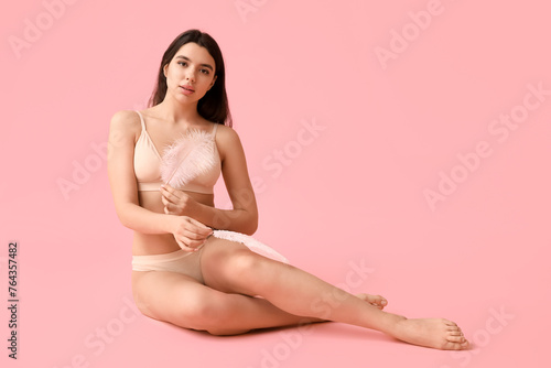 Pretty young woman with soft feathers sitting against pink background. Epilation concept