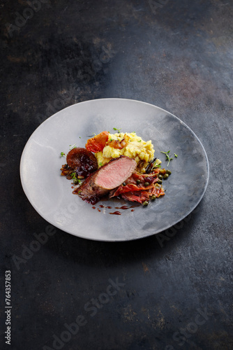 Traditionell gebratenes Wildhasen Rücken Filet mit Pflaumen, Kapern und Kartoffelsalat in Rotweinjus serviert als Nahaufnahme auf einem Nordic Design Teller 