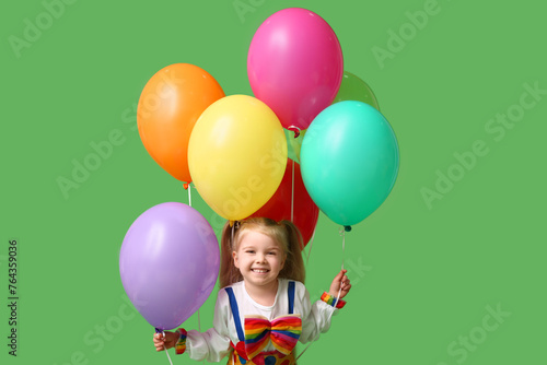 Cute little girl in clown costume with balloons on green background