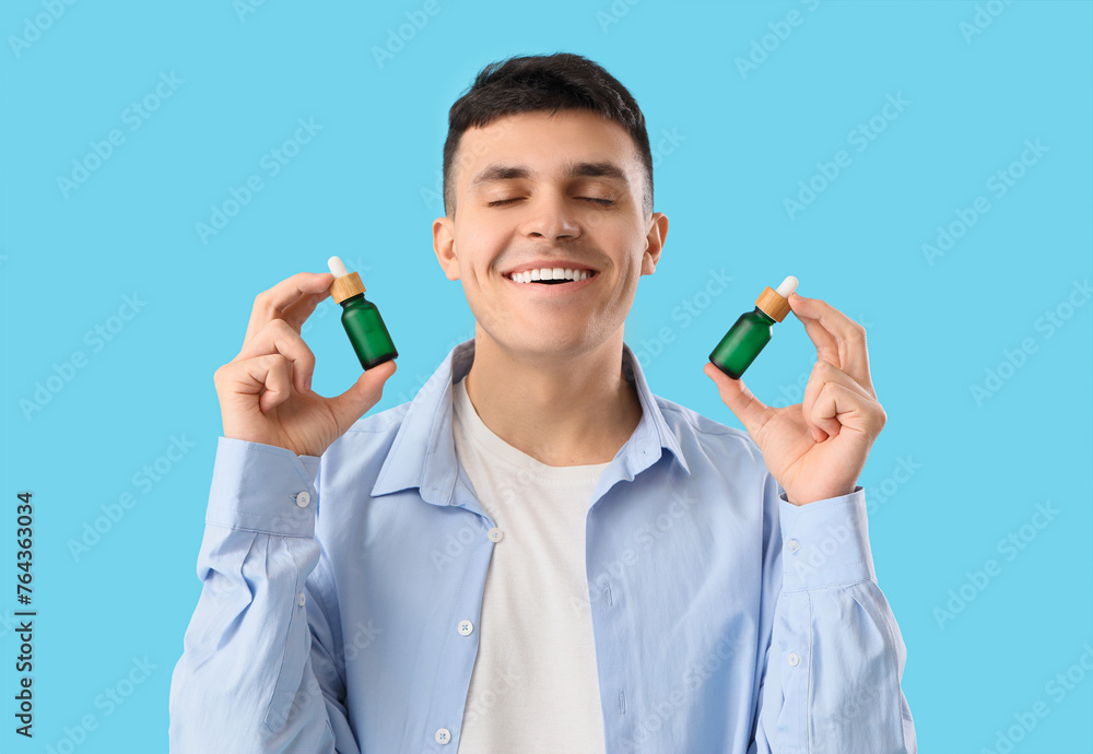 Young man with bottles of CBD oil on blue background, closeup Young man with bottles of CBD oil on blue background, closeup