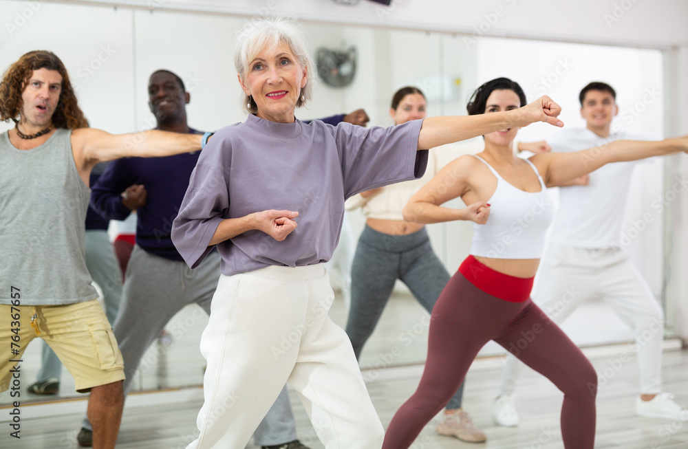 Mature woman rehearsing modern dance with group in dance school