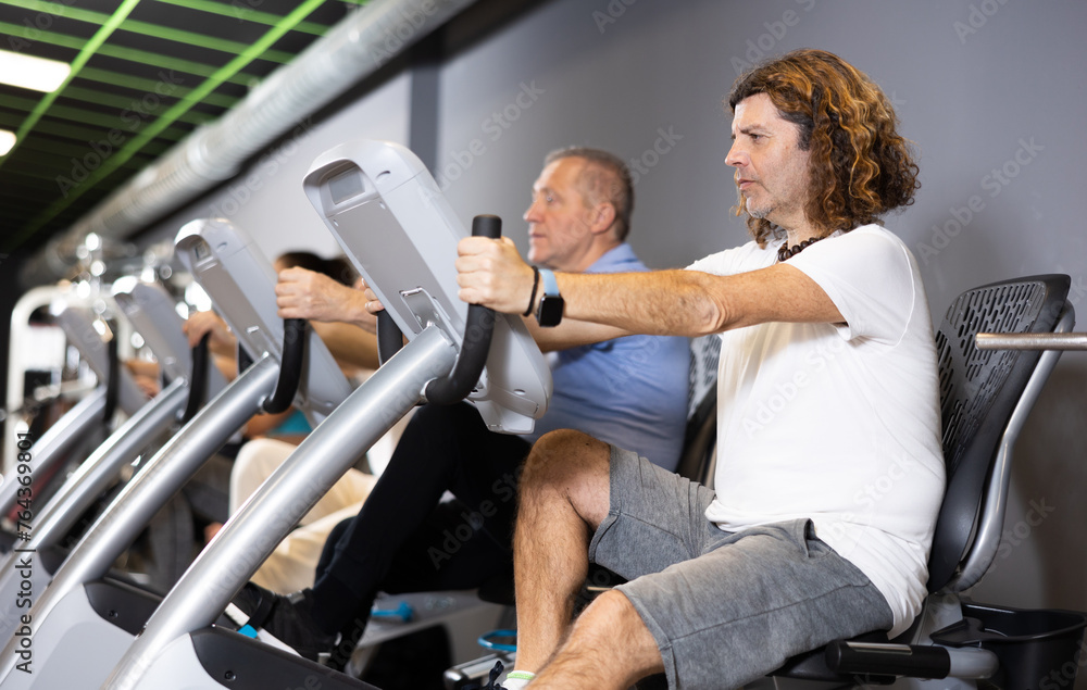 Group of people of different ages are engaged in cardio equipment in the gym
