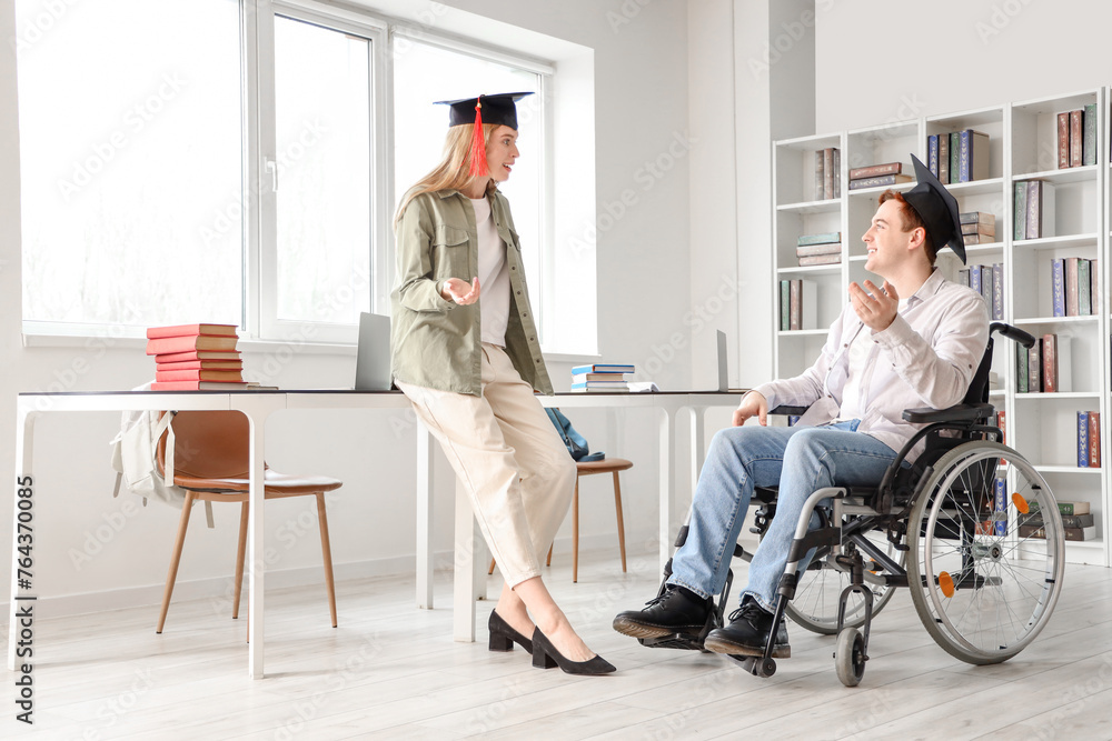 Male graduate in wheelchair chatting with his classmate at university Male graduate in wheelchair chatting with his classmate at university