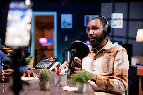 African American influencer in the studio, using a high-tech microphone for an internet program on a livestreaming channel. Man doing a podcasting session with quality streaming recording equipment.