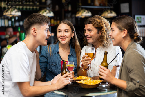 Cheerful young adult friends having fun together in vintage pub, talking and drinking beer at table