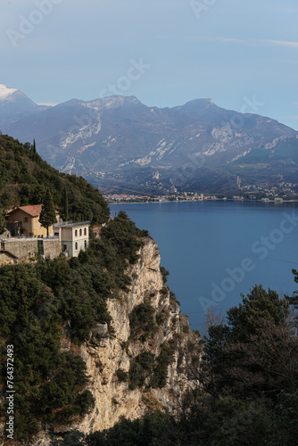 lake view with the city and mountains behind it, the lake horizon, blue sky, clear water, white rocks on one side, small sailboats near the shore, a distant mountain range with snowcapped peaks
