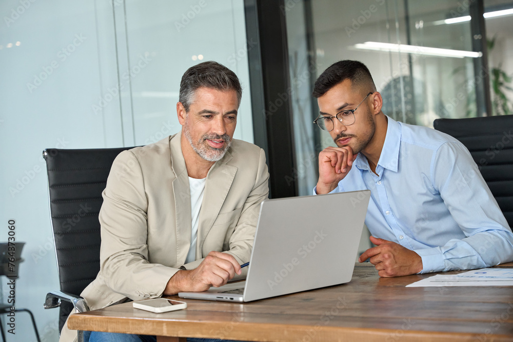 Two busy professional business men working together talking using laptop in office. Male manager and employee looking at computer discussing investment business project analysis at office meeting. Two busy professional business men working together talking using laptop in office. Male manager and employee looking at computer discussing investment business project analysis at office meeting.