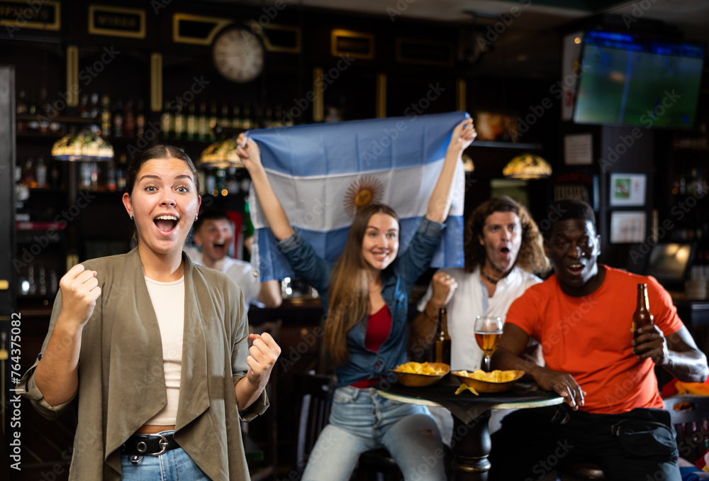 Emotional diverse soccer supporters holding the flag of Argentina and enjoing beer and potato chips, spending time together in the pub