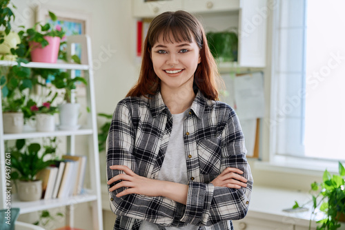 Portrait of smiling female teenager looking at camera with crossed arms in home