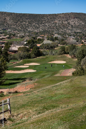 View from tee box of par 3 hole with golfers putting on putting green with Sedona, Arizona landscape 